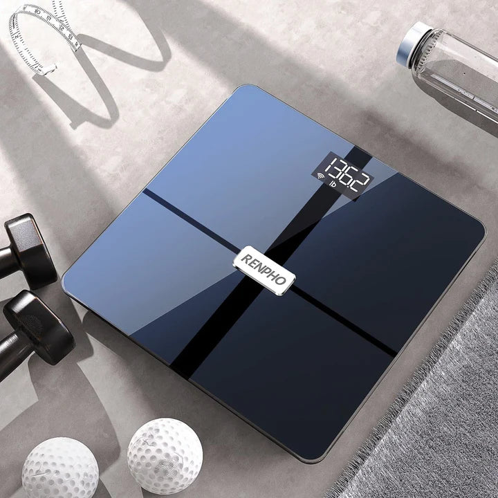 A modern, Renpho Elis Aspire Smart Body Scale displaying a weight of 132.5 pounds, centered on a neutral-toned tiled floor beside other fitness accessories: two dumbbells, golf balls, and a water.
