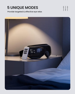 An Eyeris 1 Eye Massager by Renpho with a digital display sits on a bedside table beside a lit lamp, with its remote control next to it. The setting suggests nighttime use, highlighted by the dimly lit room.
