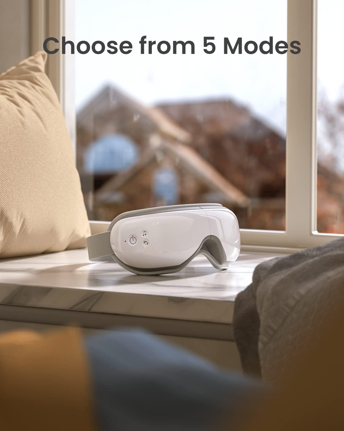A Renpho Eyeris 1 Eye Massager rests on a windowsill, backlit by a sunny view of a house with an autumnal tree. The image highlights "choose from 5 modes" text, emphasizing the eye massager's features.