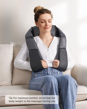 A woman sits on a couch, enjoying a Renpho U-Neck 2 Neck & Shoulders Massager with deep kneading massage nodes. She wears a white v-neck sweater and blue jeans, eyes closed in relaxation. The massager